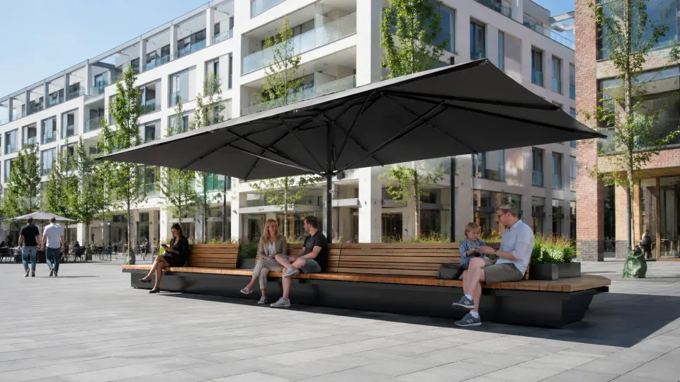 Dunkler Großschirm über einer langen Holzsitzbank mit Pflanzkästen auf einem neuen Stadtplatz