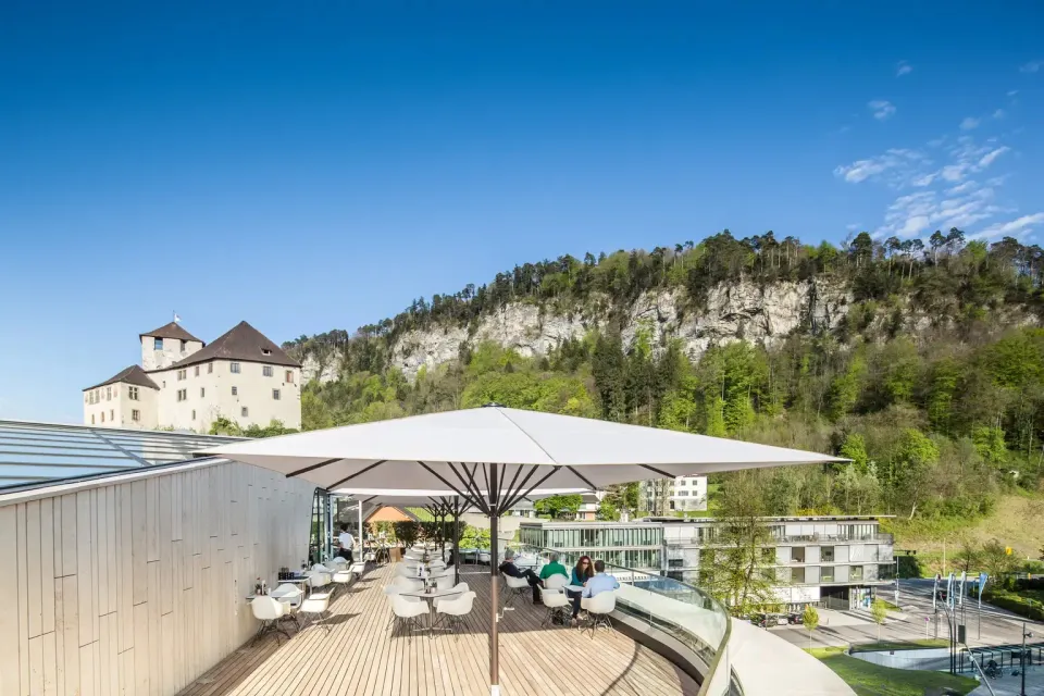 Großer heller Schirm über einer Terrasse mit Blick auf Burg und Felswand