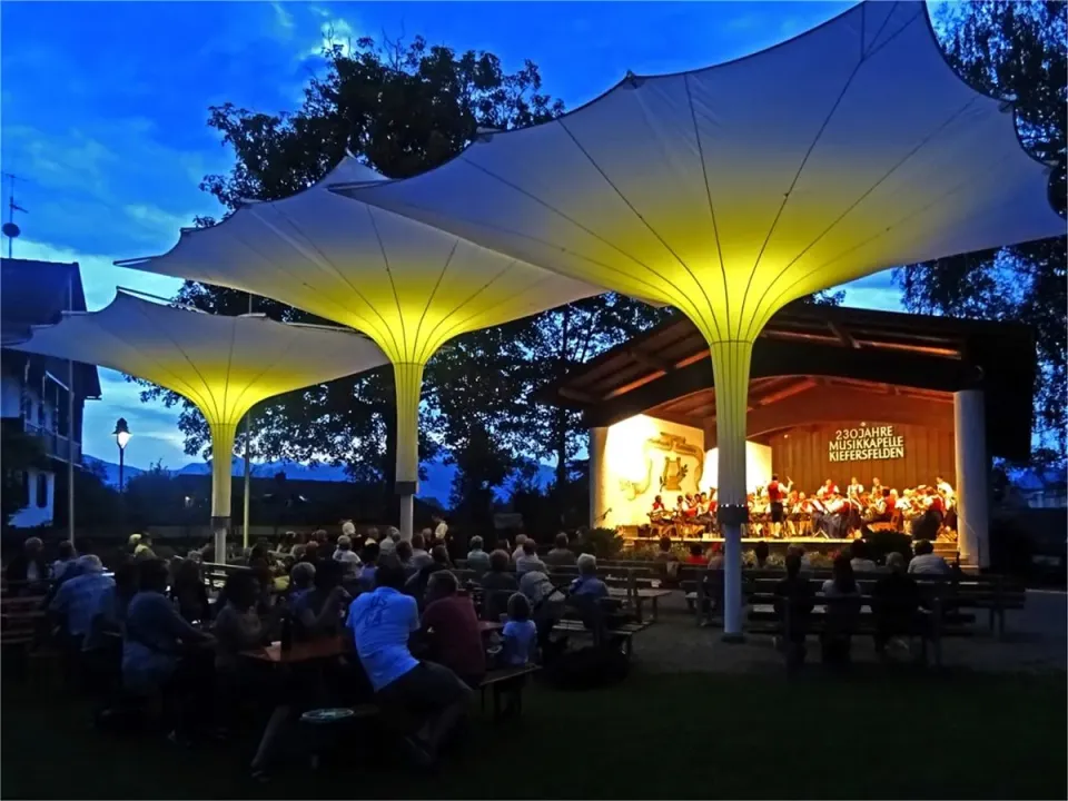 Gelb beleuchtete Tulpenschirme über Sitzreihen bei einem Konzert am Abend