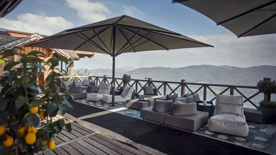 Großschirme über einer möblierten Terrasse mit Blick auf See und Berge.