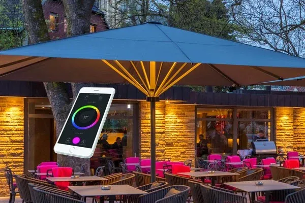 Großschirm mit LED-Beleuchtung vor einem Restaurant, Lichtfarbe wird auf einem Smartphone gewählt