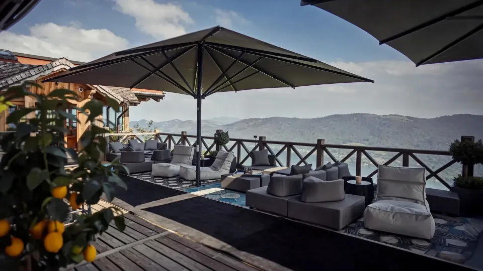 Großschirme über einer möblierten Terrasse mit Blick auf See und Berge