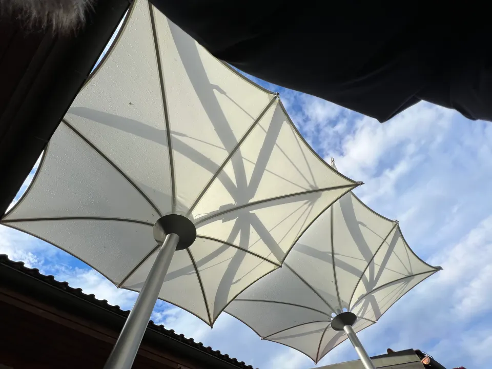 Zwei fest verspannte weiße Trichterschirme von unten, dahinter Himmel und ein Ziegeldach