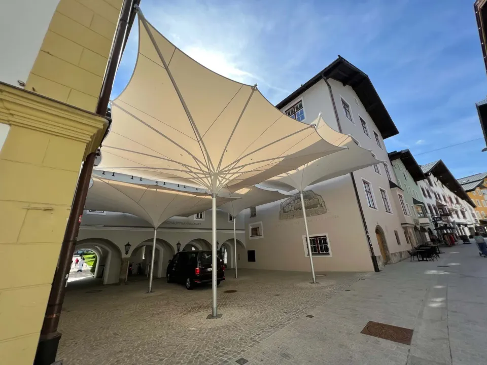 Verfahrbare Trichterschirme im Format 7 × 7 m über Innenhof und Gasse in Kitzbühel, darunter ein geparktes Auto