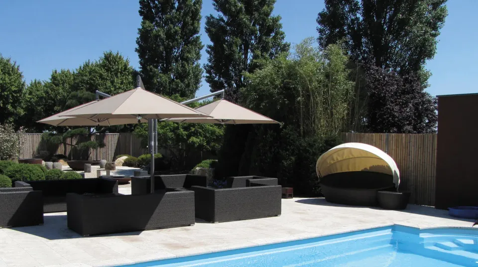 Zwei Ampelschirme mit seitlichem Mast und taupefarbenem Dach über einer Lounge mit dunklen Sofas an einem Pool
