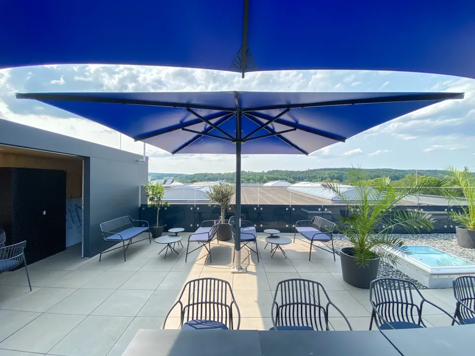 Blaue Großschirme über einer Dachterrasse mit Loungemöbeln und Palmen