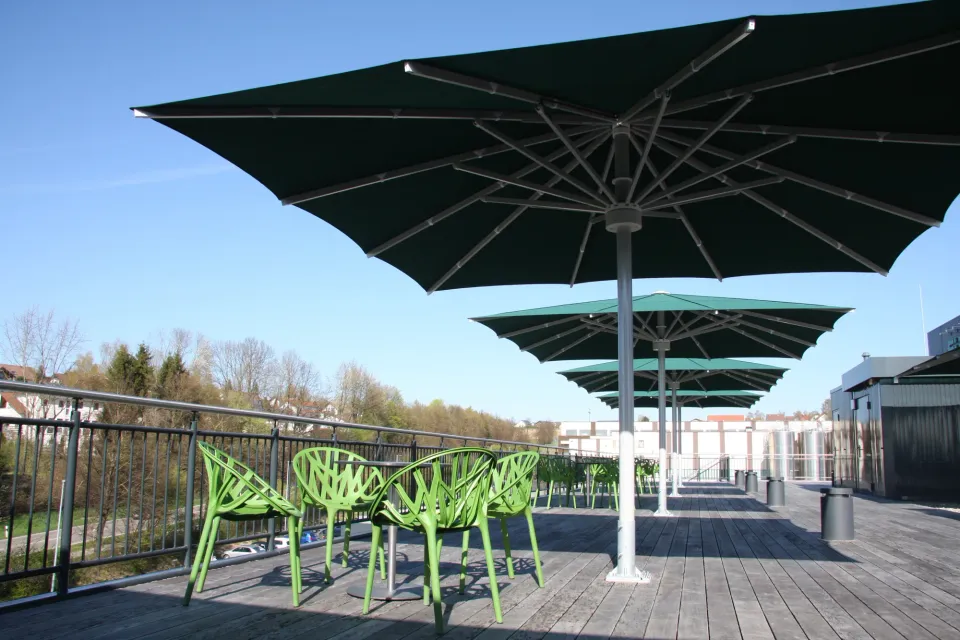 Dunkelgrüne Großschirme in einer Reihe über einer Dachterrasse mit Holzdeck und grünen Stühlen