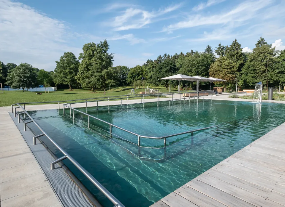 Gruppe heller Großschirme am Rand eines Freibad-Schwimmerbeckens, Holzdeck und Wiese