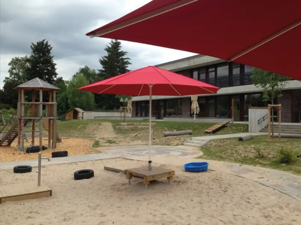 Roter Schirm über einem Sandkasten mit Spielturm auf einem Spielplatz
