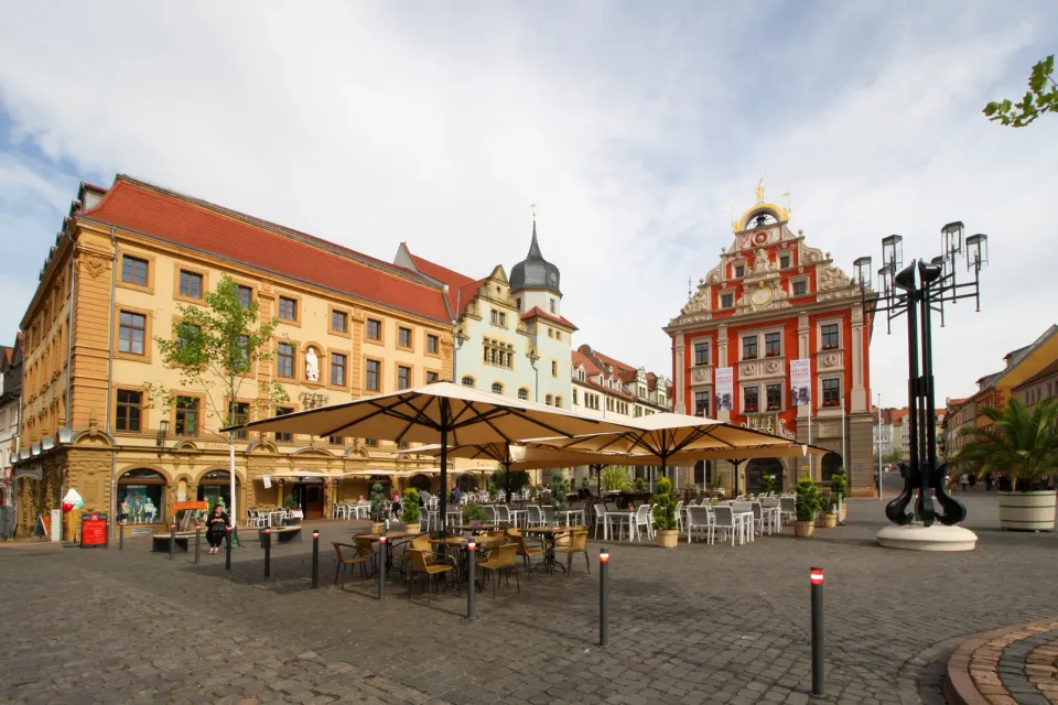 Reihe großer cremefarbener Schirme über Tischen am Marktplatz vor historischen Fassaden