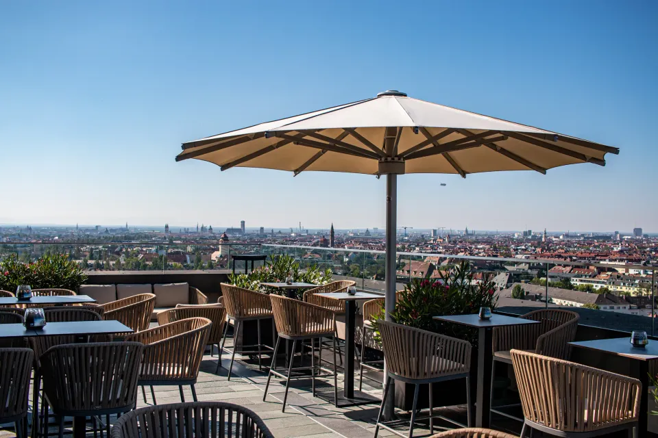 Großer cremefarbener Schirm über einer Dachterrasse mit Bar und Stadtpanorama