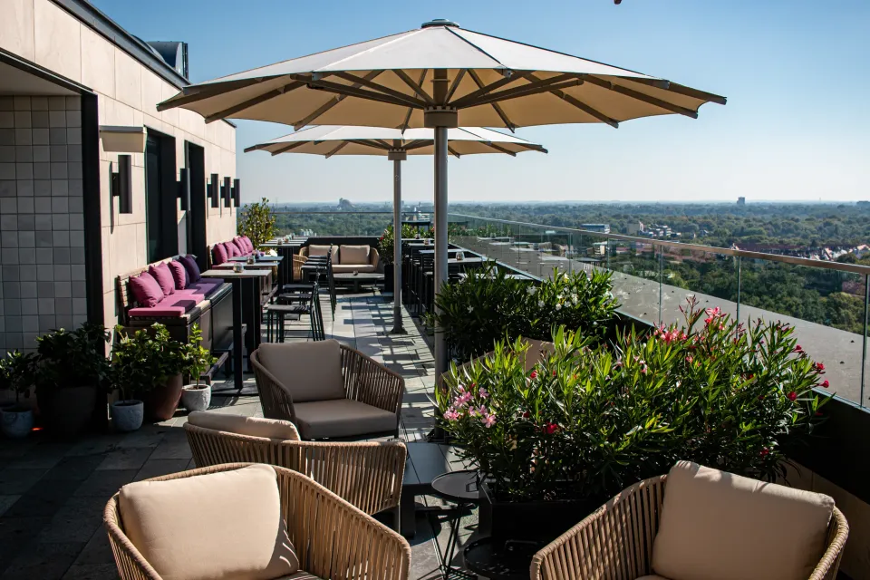 Cremefarbene Großschirme über Lounge-Sesseln auf einer Dachterrasse mit Glasbrüstung