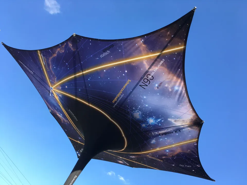 Dunkelblauer quadratischer Trichterschirm mit großflächigem Sternmotiv, goldenen Linien und Schriftzug vor blauem Himmel.