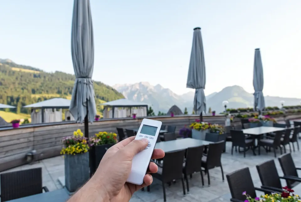 Hand mit Funksender, im Hintergrund mehrere geschlossene Großschirme auf einer Terrasse