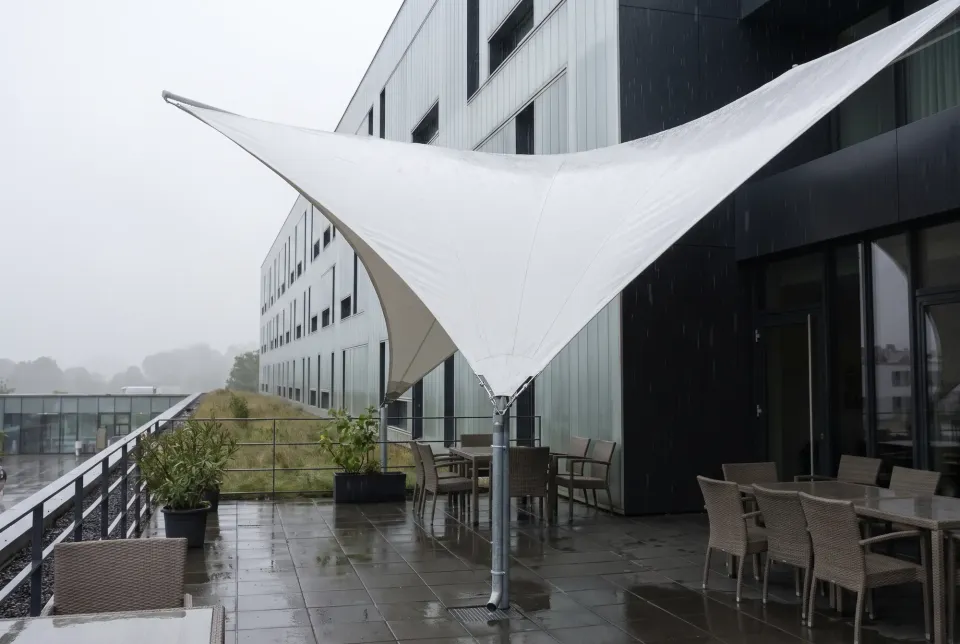 Weißes Sonnensegel an einem Mast und am Gebäude über einer Terrasse