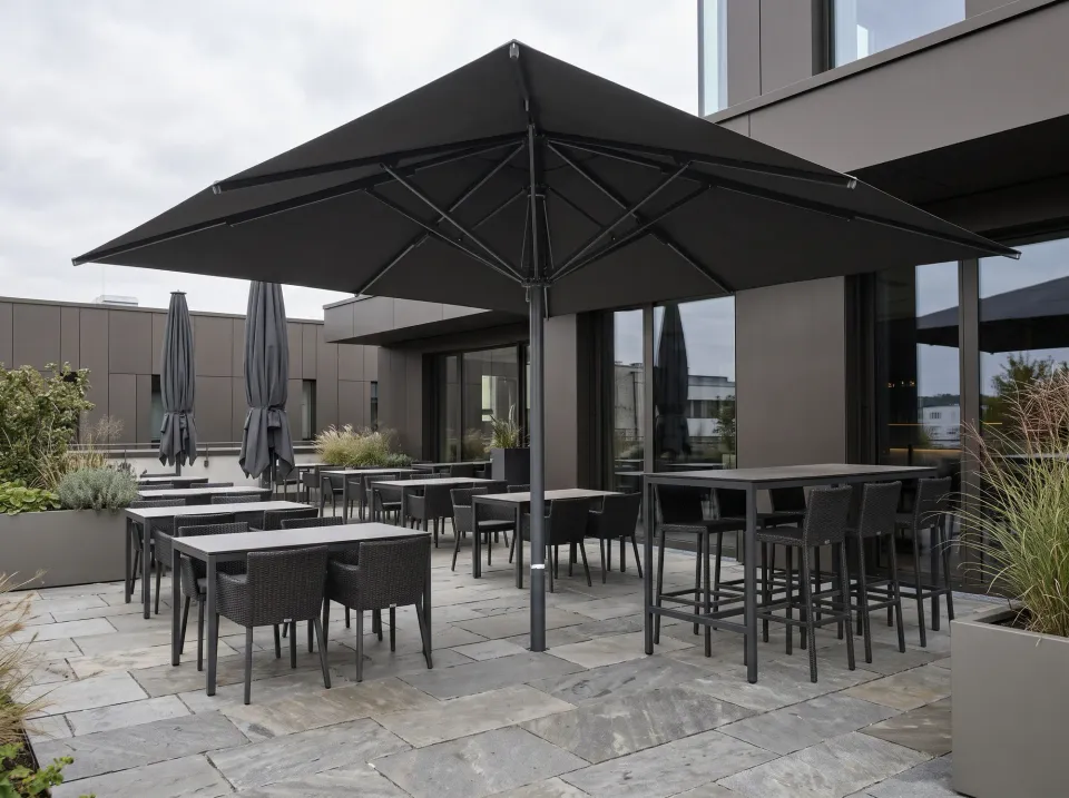 Großschirm mit anthrazitfarbenem Mast und dunklem Schirmdach hoch über den Tischen und Stühlen einer Terrasse