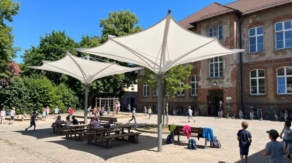 Drei weiße Membran-Trichterschirme auf einem Schulhof vor einem Backsteingebäude, spielende Kinder